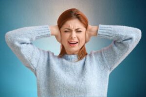 Person covering ears due to tinnitus symptoms during consultation in Estero & Naples, FL
